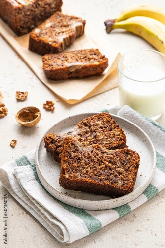 Pieces of american homemade sliced banana bread with chopped walnuts, chocolate and cinnamon on light background. Breakfast concept with milk. Vegan healthy food. Selective focus.