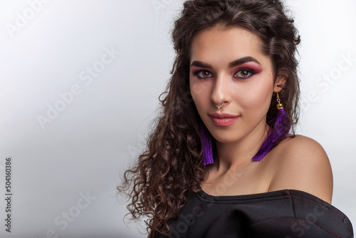 gorgeous young woman with braun glossy skin curly hair and professional make up. Indian female model dressed in black evening dress posing indoor on the white studio backgroud and looking at camera 