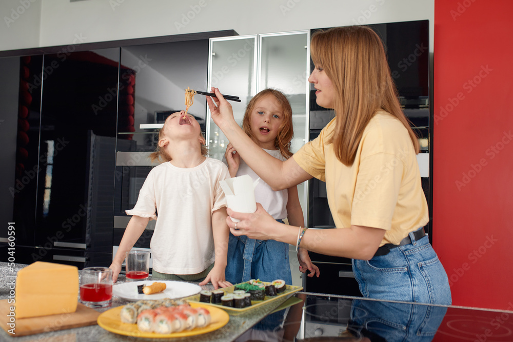 Beautiful caucasian mom and two daughters eating rolls and sushi at family lunch at home. Delivery food. Traditional japanese food.