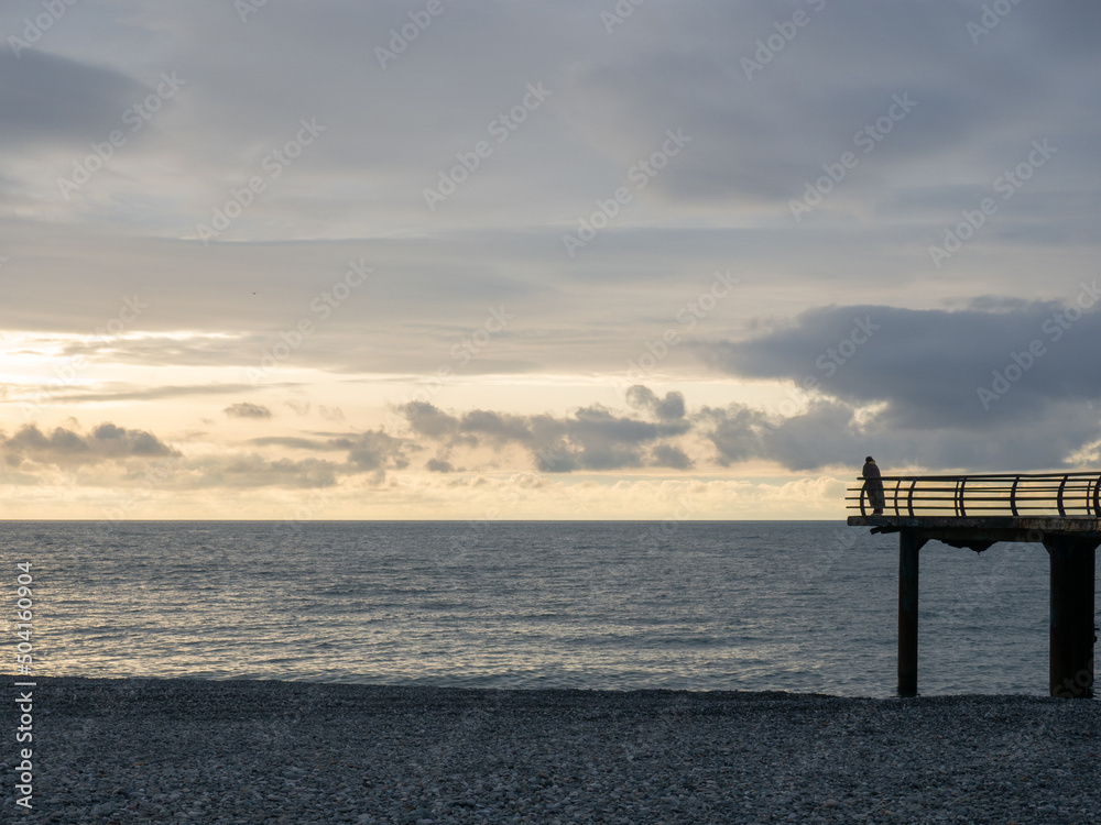 Silhouette of a man on the pier against the backdrop of sunset. Beautiful landscape. Orange sunset.
