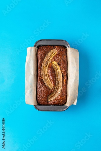 Traditional American homemade banana bread with chopped walnuts, chocolate and cinnamon in loaf pan on blue background. Fruit cake. Healthy vegan desserts concept. Top view, copy space.