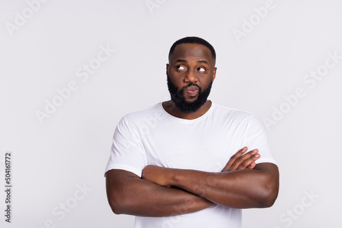 Photo of attractive doubtful guy dressed casual t-shirt arms crossed looking empty space isolated white color background