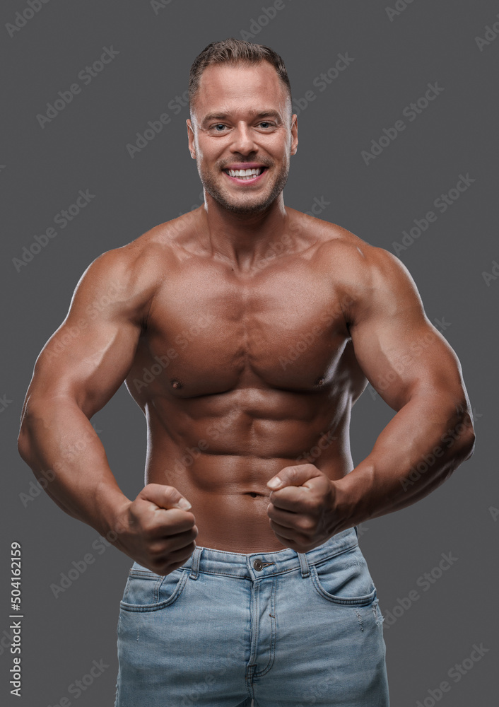 Studio shot of handsome guy with muscular build dressed in jeans posing against grey background. Studio shot of handsome guy with muscular build dressed in jeans posing against grey background.