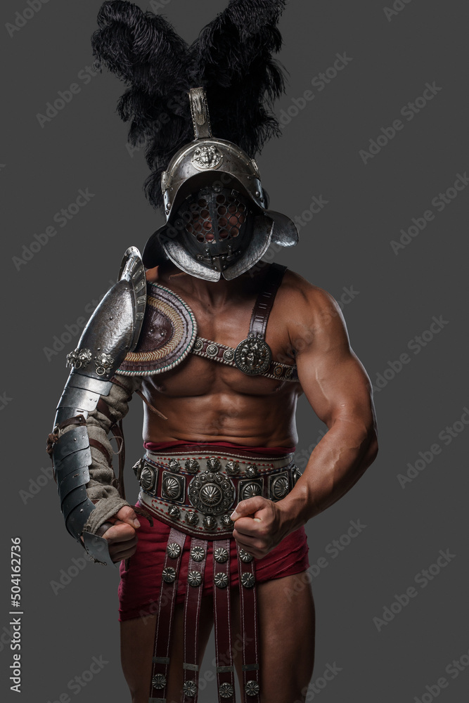 Shot of muscular ancient gladiator with plumed helmet posing against gray background.