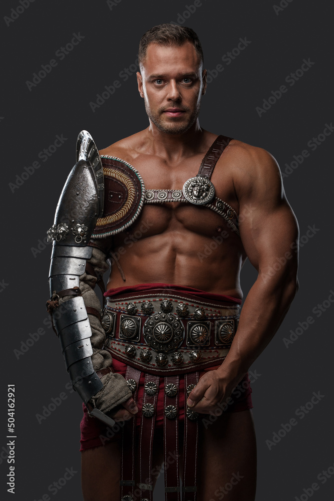 Shot of brutal roman gladiator dressed in light armor staring at camera against gray background. Shot of brutal roman gladiator dressed in light armor staring at camera against gray background.