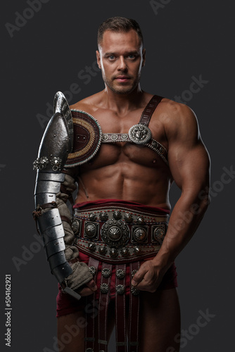 Shot of brutal roman gladiator dressed in light armor staring at camera against gray background.