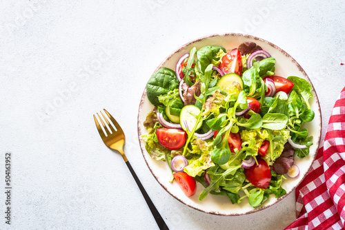 Green salad, veggie dish. Fresh salad leaves and vegetables in white plate. Healthy vegan food, diet food. Top view image.