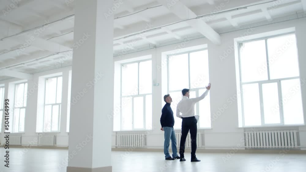 Businessman and realtor discuss contract while inspecting an office space for rent, side view. Realtor shows client rental space Businessman and realtor discuss contract while inspecting an office space for rent, side view. Realtor shows client rental space