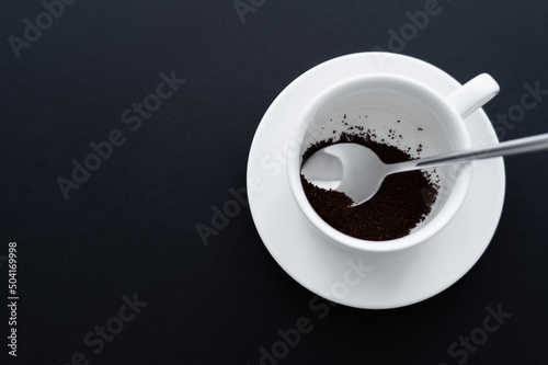 Fotografiet top view of ground coffee in cup with spoon on black.
