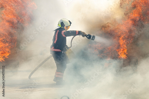The hero firefighter stands among the smoke and fire and extinguishes the fire with a stream of water.. firefighter extinguishes a fire photo