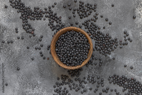 Wooden bowl of dry black lentils beans on grey table top view, protein source for vegetarian diet