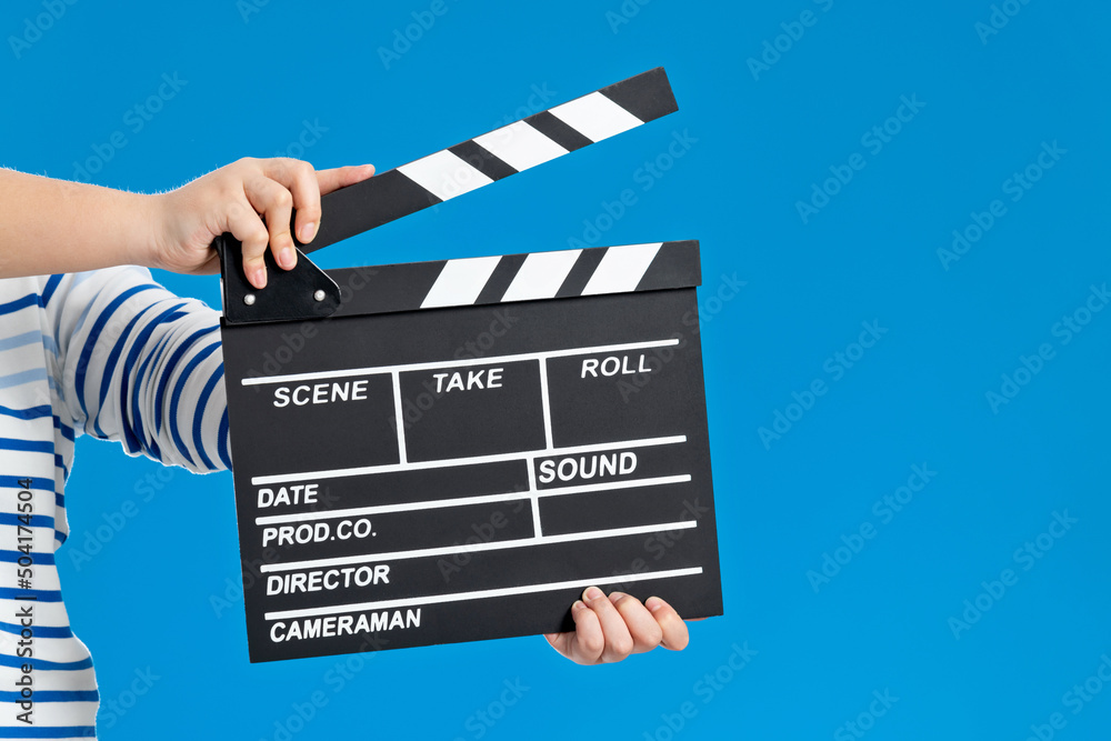 Obraz premium Woman hands holding cinema clapperboard on blue background