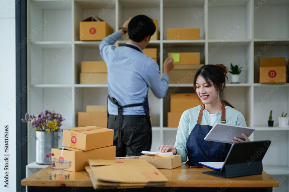 startup small business owner working with tablet at workplace. freelance man and woman seller check product order, packing goods for delivery to customer. Online selling, e-commerce, shipping concept startup small business owner working with tablet at workplace. freelance man and woman seller check product order, packing goods for delivery to customer. Online selling, e-commerce, shipping concept