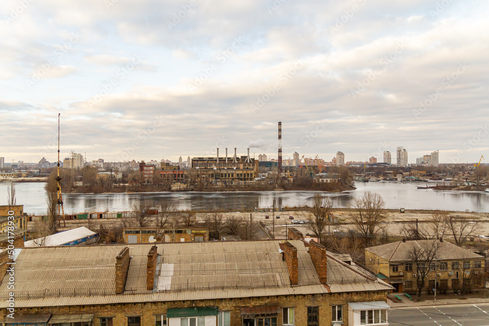 Obraz premium Kyiv, Ukraine – February 06, 2016: A beautiful panorama of Podil region during sunset. Aerial view on residential and industrial areas. Different architectural style. Historical area, Dnipro river.