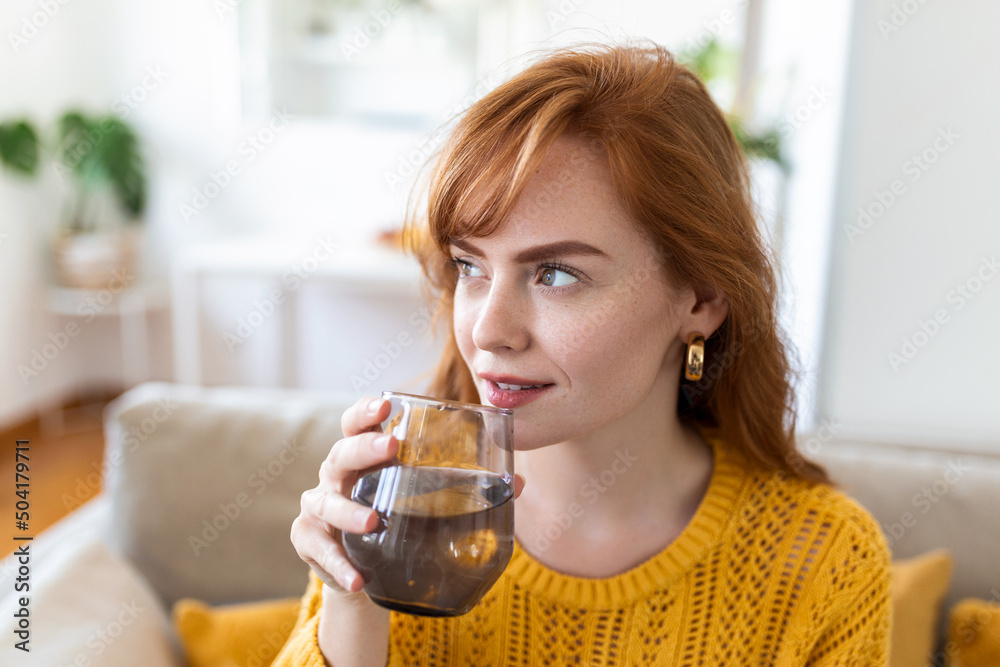 Happy young woman smiling while holding a glass of water at home. Woman on living room sofa Relaxed and Smiling While Drinking glass of water. Health benefits of drinking enough water