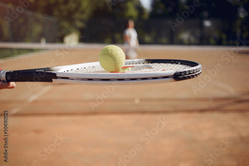 Cropped photo of racket with ball and blurred second player