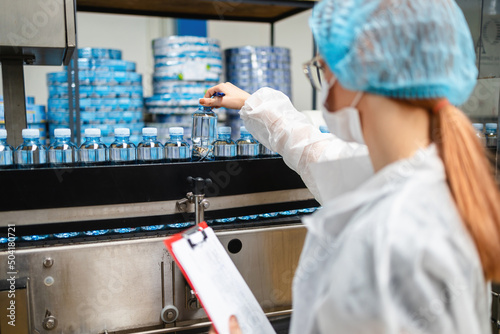 Female worker with protective face mask working in medical supplies research and production factory and checking canisters of distilled water before shipment. Inspection quality control. photo