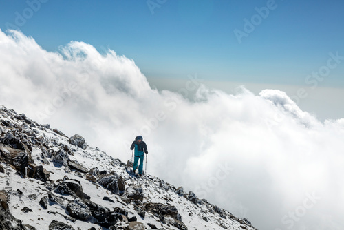 Climber tourist hikes on frozen rocks and stones over clouds in big mountains