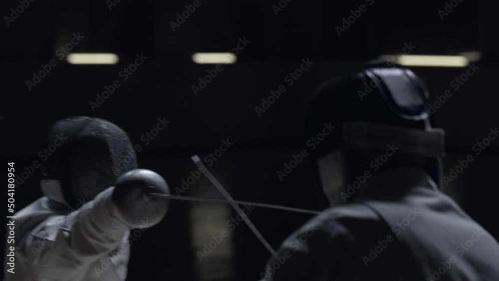 Two professional male fencers having a sabre fight in against dark background Two professional male fencers having a sabre fight in against dark background