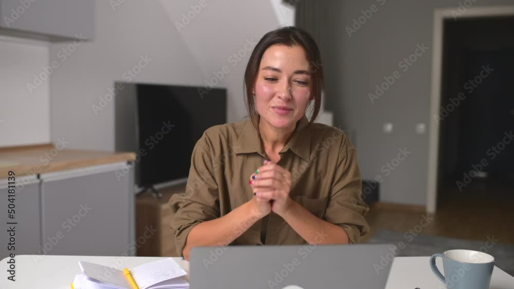 Smiling asian woman in casual wear sitting in the living room, using laptop for video connection, talking to her friend or colleagues on the distance, waving, staying in touch during pandemic Smiling asian woman in casual wear sitting in the living room, using laptop for video connection, talking to her friend or colleagues on the distance, waving, staying in touch during pandemic