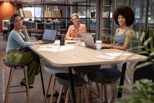 Portrait of happy multiracial female advisors sitting at desk in modern workplace