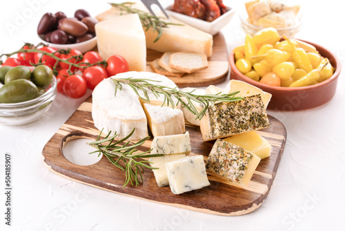 Valokuva Wooden cheese board with variety of cheeses served with olives, cherry tomatoes, pickled baby peppers on white table background