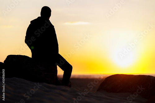Silhouette eines Mannes sitzend auf Stein im Sonnenuntergang