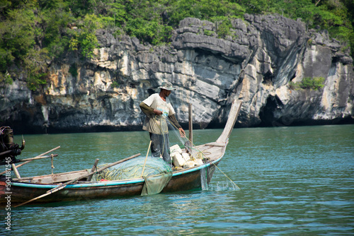 Thai man fisher people sailing wood long tail boat fishery floating in sea use net catch fishing marine and fish in ocean at Mu Ko Petra National Park at Pak Bara on April 12, 2022 in Satun, Thailand