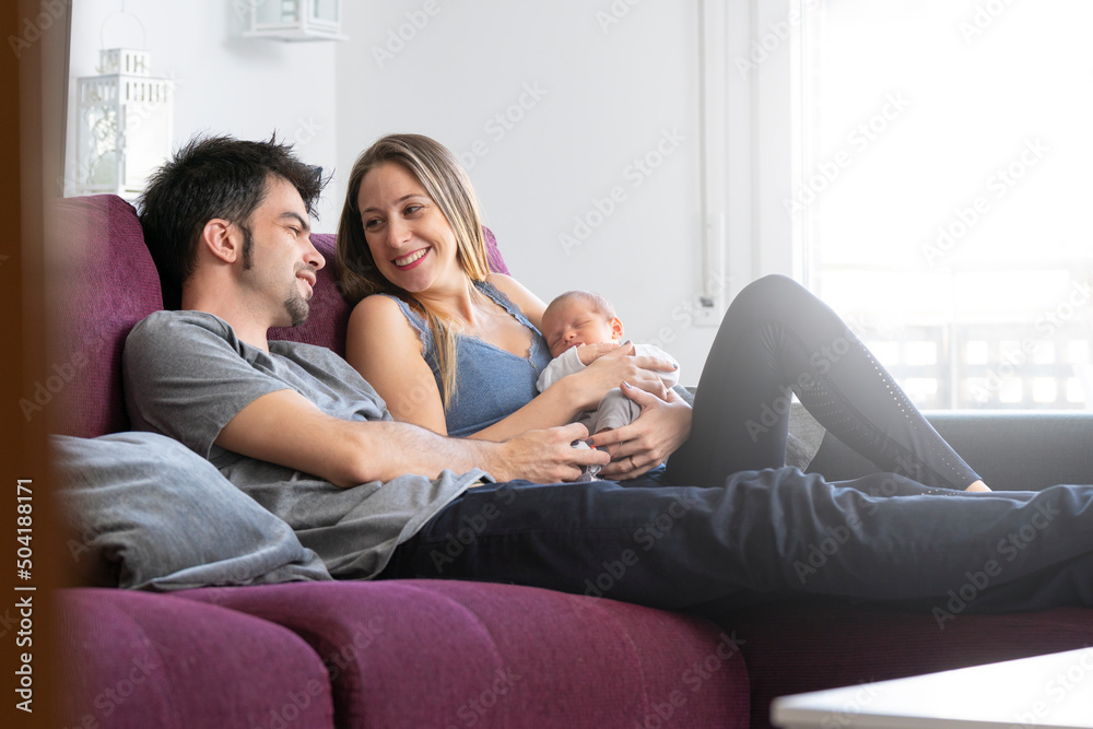 A couple of parents sitting on a sofa in the living room with their newborn baby