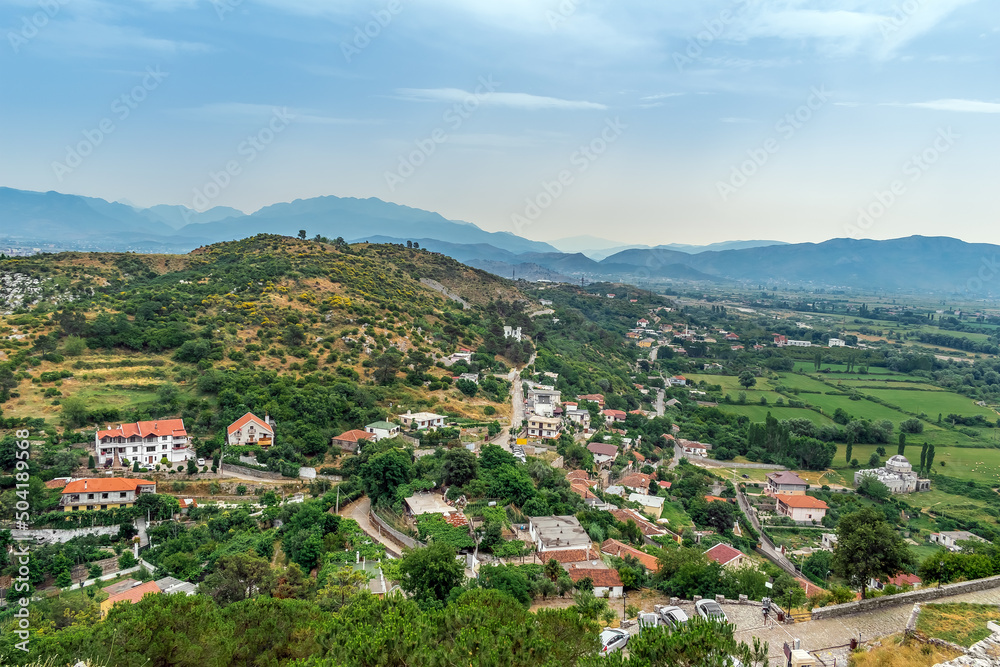 Aerial view of the countryside among the mountains in the suburbs of Shkoder, Albania. Rural buildings with red roofs among the summer greenery near the hill