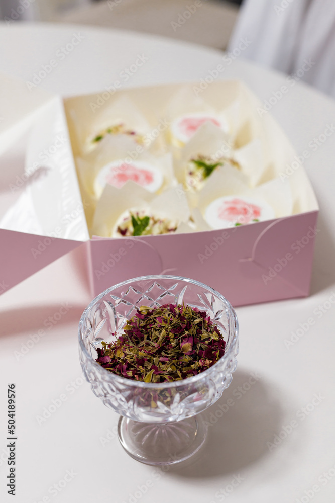 Vase of dried rose flower petals for pastry decoration. Aromatic dressing, pink box of cupcakes on background. Homemade sweet cakes Vase of dried rose flower petals for pastry decoration. Aromatic dressing, pink box of cupcakes on background. Homemade sweet cakes