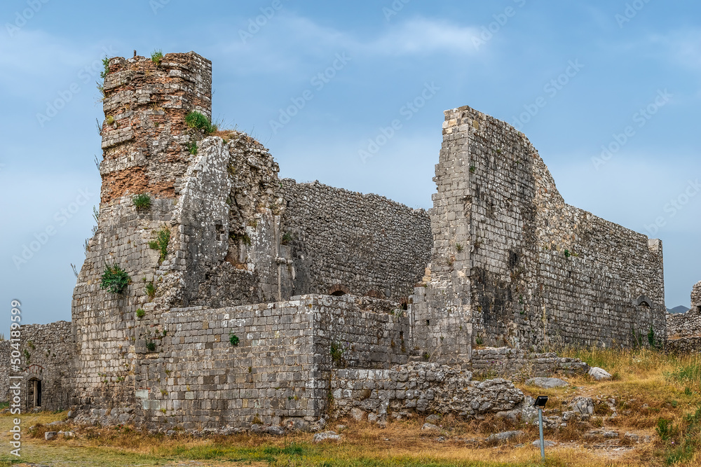 Ruins of an ancient tower in Rozafa Castle, Albania. Remains of a medieval stone fortress on a lawn with yellow-green dry grass against a blue sky