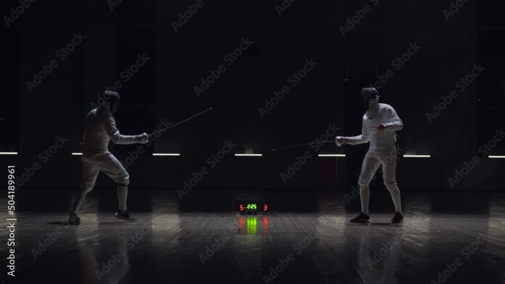 Two professional male fencers having a sabre fight in against dark background Two professional male fencers having a sabre fight in against dark background