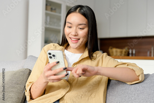 Obraz na plátně Cute asian woman looking at the smartphone in her hands