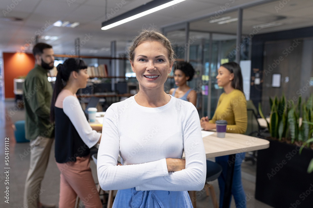 Portrait of smiling caucasian female advisor with arms crossed against team at workplace Portrait of smiling caucasian female advisor with arms crossed against team at workplace