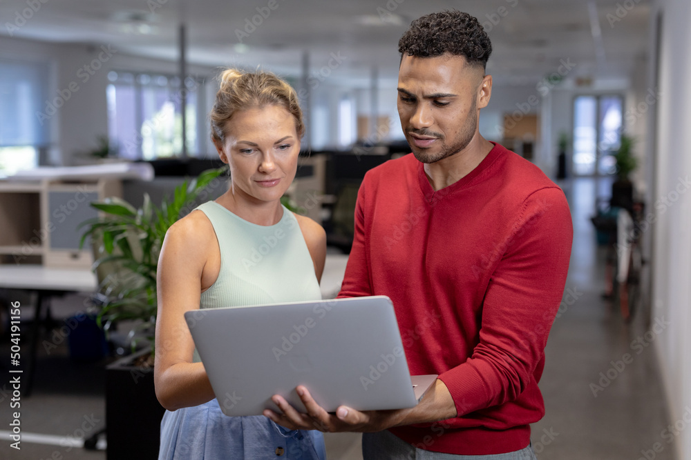 Multiracial business advisors discussing over laptop while standing at modern workplace Multiracial business advisors discussing over laptop while standing at modern workplace