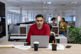 Portrait of confident hispanic male advisor with laptop at desk working in modern workplace