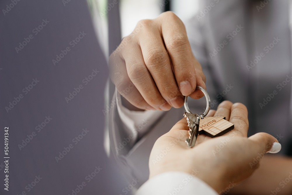 Fototapeta premium A home rental company employee is handing the house keys to a customer who has agreed to sign a rental contract, explaining the details and terms of the rental. Home and real estate rental ideas.