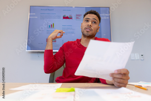 Confident hispanic male advisor pointing at television screen while giving presentation in boardroom