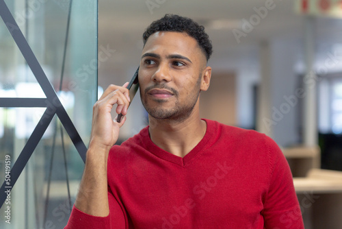 Thoughtful young hispanic businessman looking away while talking on smartphone