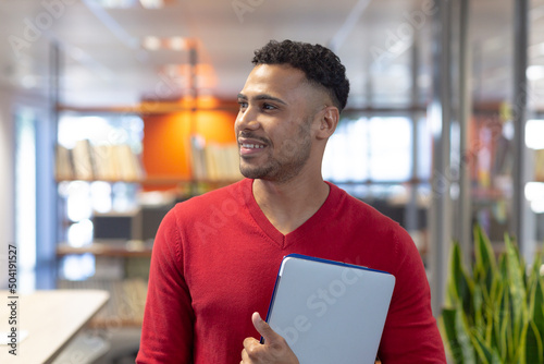Smiling hispanic male advisor looking away while holding digital tablet in modern workplace