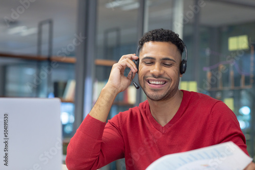 Smiling hispanic male telecaller talking through headset in modern workplace