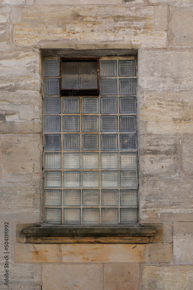 Very old glass brick window with shutters, beige and bright sand stone wall, no person