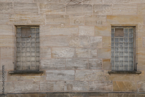 Two glass brick windows on a old beige and bright sand stone wall, no person