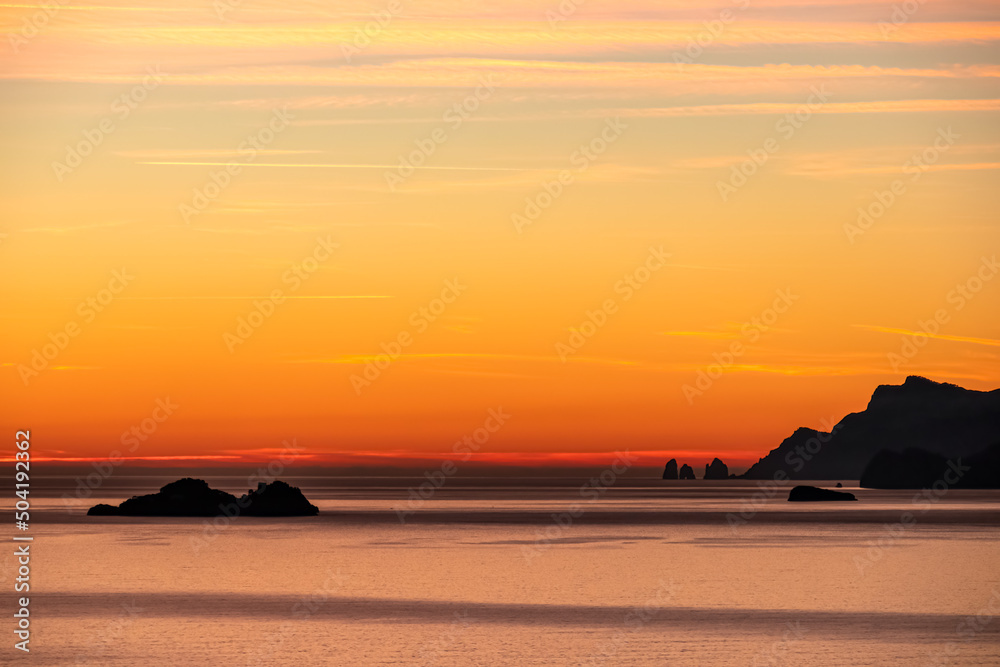 Panoramic sunset view from Praiano at Mediterranean Sea, Italy, Campania, Europe. Silhouette of Li Galli islands and coastline of Amalfi Coast. Reflection of sun beams on water surface during twilight