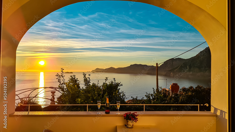 Champagne bottle with scenic sea view during sunset from luxury apartment on Mediterranean Sea. Terrace balcony with arch overlooking the coastline in Praiano, Amalfi Coast, Campania, Italy, Europe - obrazy, fototapety, plakaty 