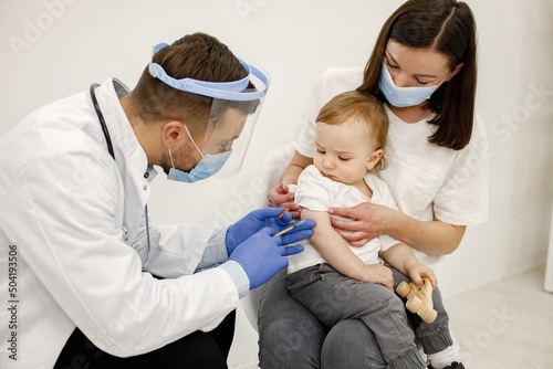 Male doctor doing a vaccination to a little boy who sitting on mother's lap © prostooleh