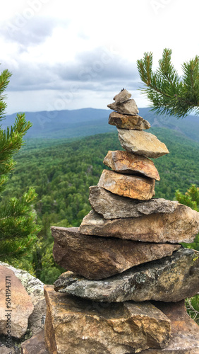 A stone pyramid in natural nature at a height, has a beneficial effect on all spheres of life. View from a high mountain to a huge area of the forest. In the frame there are pine branches on the sides