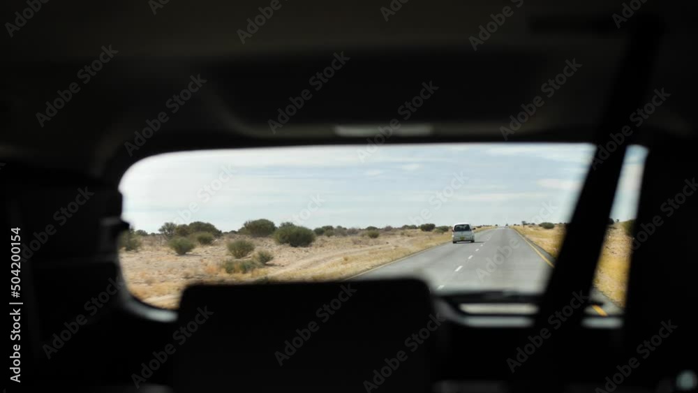 A road in Namibia with a small car driving over it, filmed through the rear window of an SUV. A road in Namibia with a small car driving over it, filmed through the rear window of an SUV.