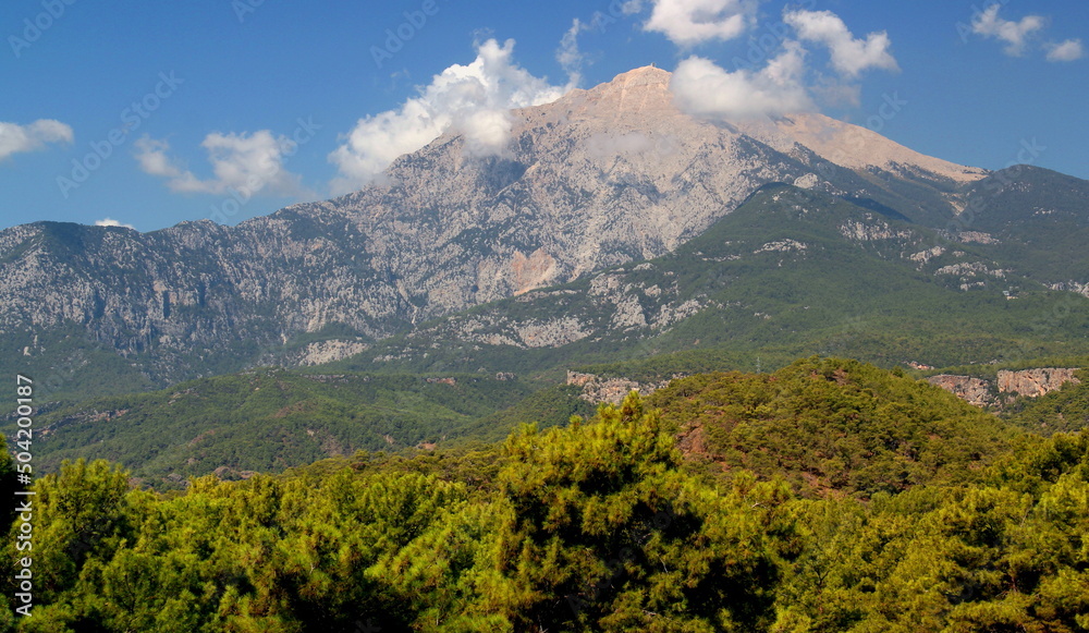Panoramic view of Tahtalı mountain, which is slightly obscured by clouds, with dense forest in the foreground near the town of Kemer, Antalya region, Turkey	